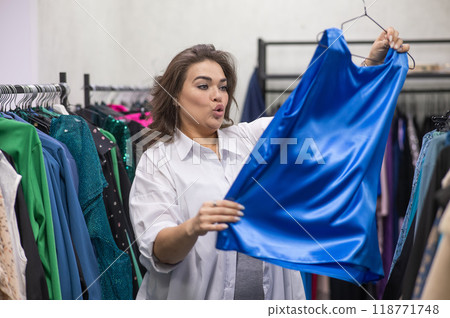 A fat woman chooses clothes in a plus size store.  118771748