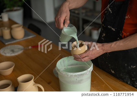 Close-up of a potter's hands glazing a pottery piece. Close-up of a potter's hands glazing a pottery piece. 118771954