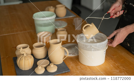 Close-up of a potter's hands glazing a ceramic mug. Close-up of a potter's hands glazing a ceramic mug. 118772000