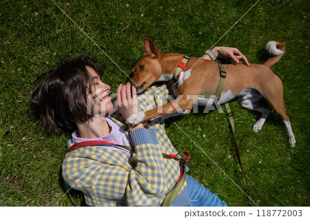 Top view of beautiful young woman and african basenji dog lying on green grass. Top view of beautiful young woman and african basenji dog lying on green grass. 118772003