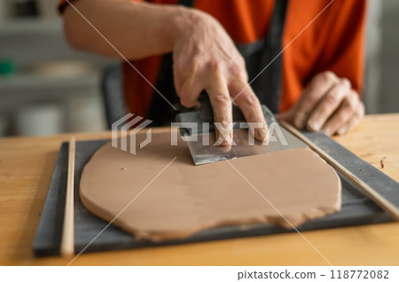 Close-up of a potter's hands cutting off a piece of rolled clay with patterns. Close-up of a potter's hands cutting off a piece of rolled clay with patterns. 118772082