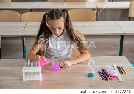 A schoolgirl conducts experiments in a chemistry lesson. Girl pouring colored liquids from a beaker. A schoolgirl conducts experiments in a chemistry lesson. Girl pouring colored liquids from a beaker. 118772248