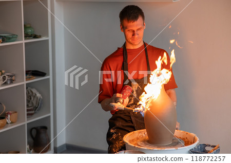 A potter burns a jug with a gas burner on a potter's wheel. A potter burns a jug with a gas burner on a potter's wheel. 118772257
