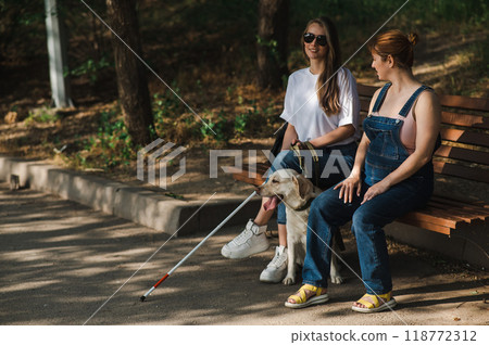 Blind caucasian woman sitting on bench with guide dog and pregnant friend.  118772312