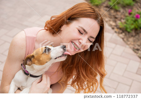 Dog jack russell terrier licks the owner in the face outdoors. Girl with braces on her teeth.  118772337