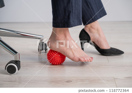 Business woman massages her feet on a massage ball with spikes. 118772364
