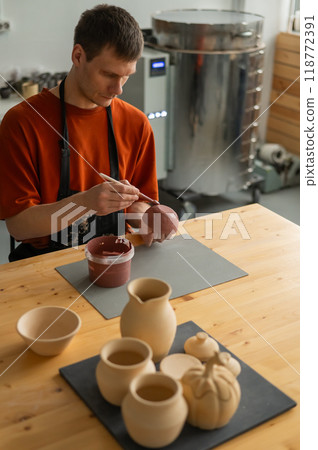 Potter paints ceramic dishes with a brush. Vertical photo. Potter paints ceramic dishes with a brush. Vertical photo. 118772391