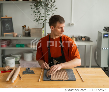 A potter cuts a piece of rolled clay with patterns.  118772476
