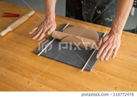Close-up of potter's hands rolling out clay.  118772478
