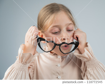 Portrait of a cute little girl blowing on heart-shaped glasses on a white background. Portrait of a cute little girl blowing on heart-shaped glasses on a white background. 118772545