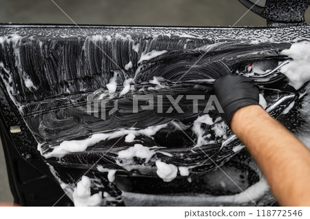 A man cleans the interior of a car with foam and a brush. Clean the door trim. A man cleans the interior of a car with foam and a brush. Clean the door trim. 118772546