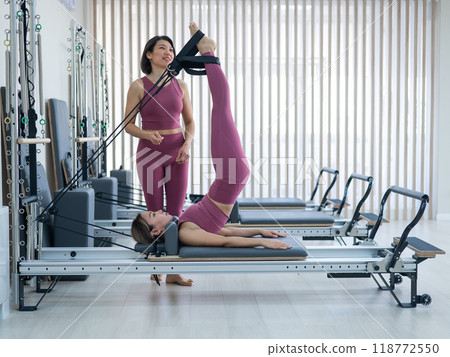 Asian woman doing pilates with trainer on reformer.  118772550