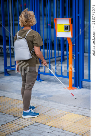 An elderly blind woman goes to a button to call help for people with disabilities. Vertical photo.  118772572
