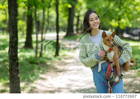 A young beautiful woman holds a dog in her arms for a walk. non-barking african basenji dog.  118772607