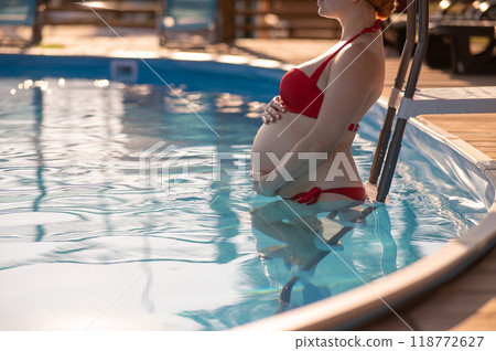 Pregnant red-haired woman in the pool in a red bikini.  118772627