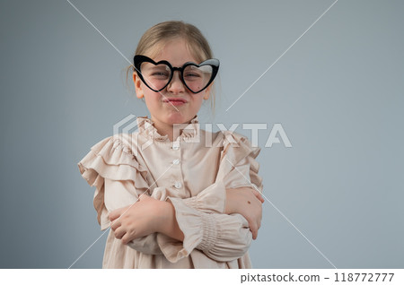 Portrait of a cute little girl grimacing wearing heart-shaped glasses on a white background.  118772777