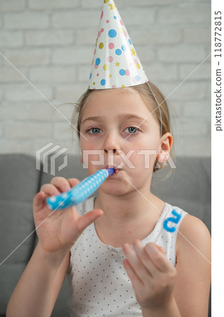Portrait of a little Caucasian girl with a festive cap at her birthday party.  118772815
