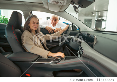 An elderly couple chooses a new car at a car dealership. Mature woman driving.  An elderly couple chooses a new car at a car dealership. Mature woman driving.  118772825