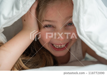 Portrait of a cute little girl laughing and hiding under the blanket. Portrait of a cute little girl laughing and hiding under the blanket. 118772890