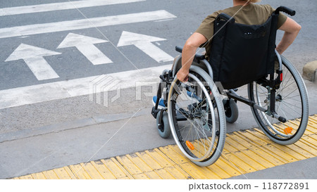 Rear view of an elderly Caucasian woman in a wheelchair crosses the road at a pedestrian crossing. Rear view of an elderly Caucasian woman in a wheelchair crosses the road at a pedestrian crossing. 118772891