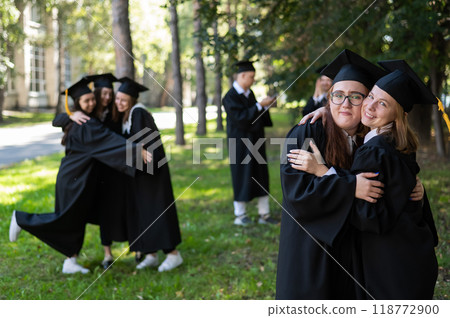 A group of graduates in robes congratulate each other on their graduation outdoors. A group of graduates in robes congratulate each other on their graduation outdoors. 118772900