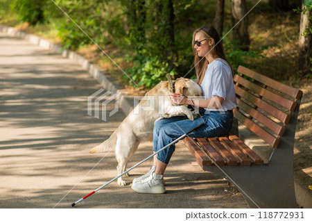 Blind young woman cuddling with guide dog while sitting on a bench.  118772931