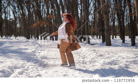 Portrait of an excited red-haired curly fat woman in the park in winter. 118772958