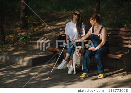 Blind caucasian woman sitting on bench with guide dog and pregnant friend. Blind caucasian woman sitting on bench with guide dog and pregnant friend. 118773038