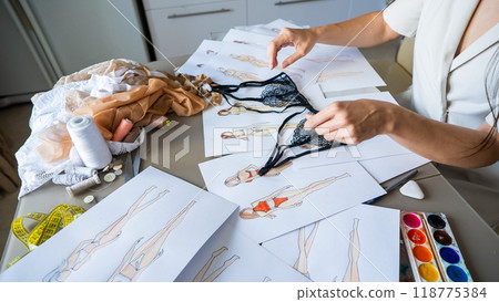 Faceless woman draws underwear sketches. Close-up of fashion designer's hands with lace bra. 118775384