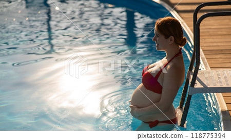 Pregnant red-haired woman in the pool in a red bikini.  118775394