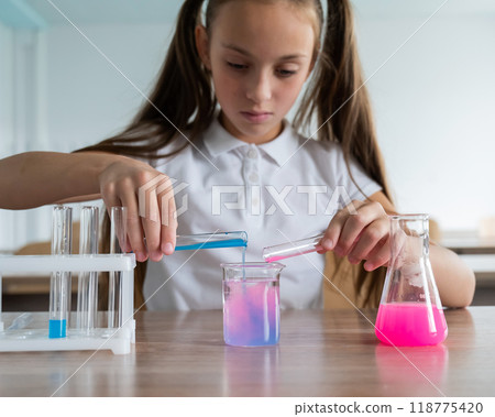 A schoolgirl conducts experiments in a chemistry lesson. Girl pouring colored liquids from a beaker. A schoolgirl conducts experiments in a chemistry lesson. Girl pouring colored liquids from a beaker. 118775420