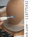 Close-up of a potter's hands firing a jug with a gas burner on a potter's wheel. Vertical photo.  118775432