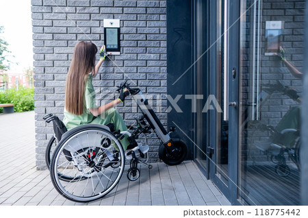 A woman in a wheelchair with an assistive device for manual control enters the entrance. Electric hand bike. 118775442