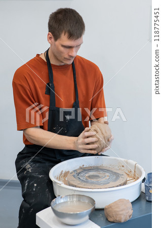 A potter kneads clay before using it on the potter's wheel. Vertical photo.  118775451