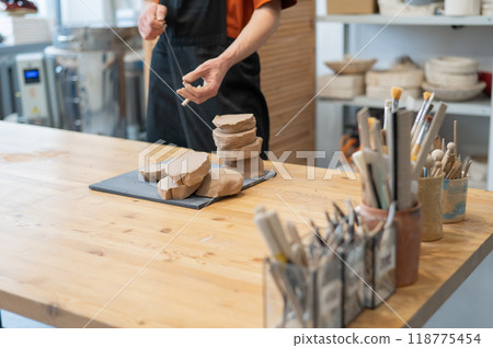 A potter cuts a piece of clay into pieces before using it in the workshop.  118775454