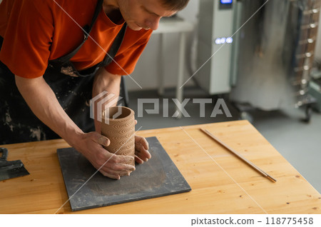 Close-up of a man's hands making a patterned cylinder out of clay.  118775458