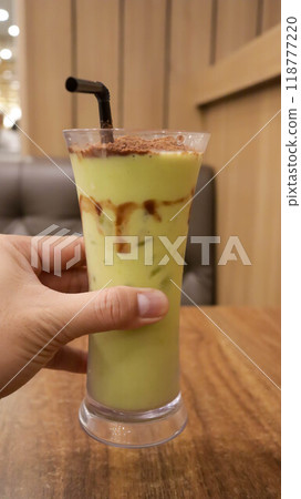 A hand holding a glass of avocado juice with sprinkle of cocoa powder topping on the table. A hand holding a glass of avocado juice with sprinkle of cocoa powder topping on the table. 118777220