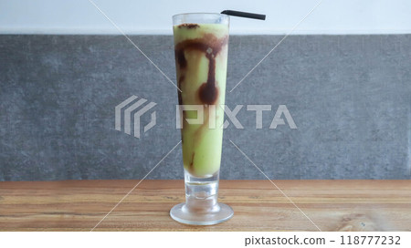 A glass of avocado juice with a little chocolate topping on the table. 118777232