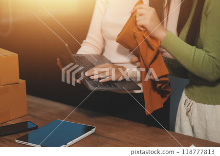 Startup SME small business entrepreneur of freelance Asian woman wearing apron using laptop and box to receive and review orders online to prepare to pack sell to customers, online sme business ideas. 118777813