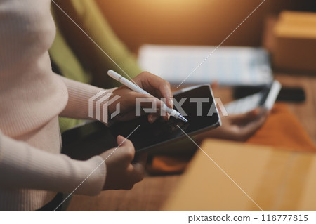 Startup SME small business entrepreneur of freelance Asian woman wearing apron using laptop and box to receive and review orders online to prepare to pack sell to customers, online sme business ideas. 118777815