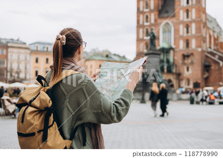 Attractive young female tourist is exploring new city. Happy girl holding a paper map on Market Square in Krakow. Traveling Europe in autumn. St. Marys Basilica 118778990