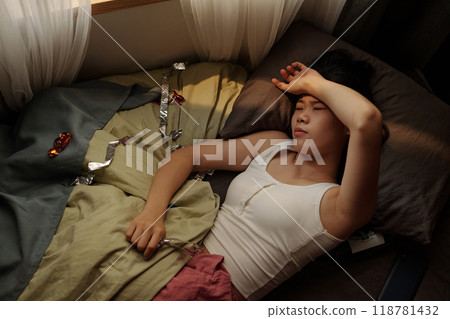 Woman with headache resting on bed 118781432