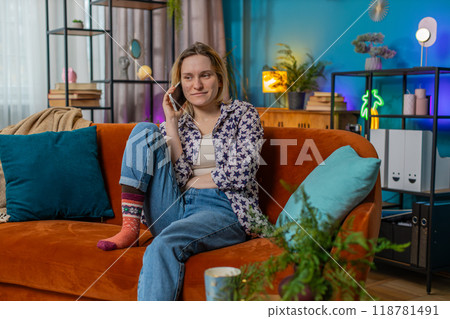 Happy young Caucasian woman making mobile phone conversation with friends sitting on couch at home 118781491