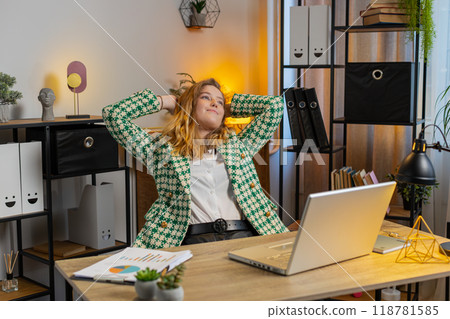 Happy businesswoman at home office desk works on laptop and stretching arms after finishing work 118781585