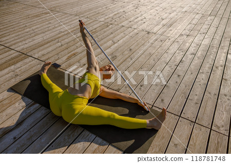 Engaging in a Flexible Yoga Pose on a Beautiful Sunrise Deck Using a Stretching Pole Engaging in a Flexible Yoga Pose on a Beautiful Sunrise Deck Using a Stretching Pole 118781748