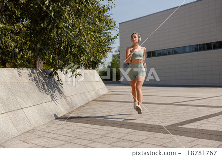 A young woman jogging outdoors in a vibrant urban setting, displaying her enthusiasm for fitness 118781767