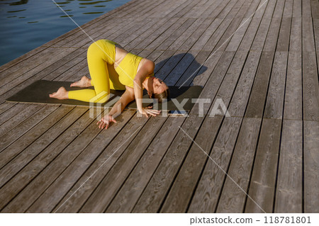 Enjoying a Yoga Practice by the Water while Dressed in a Vibrant Bright Yellow Outfit 118781801