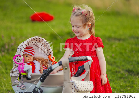 little girl plays with a doll and a stroller little girl plays with a doll and a stroller 118781962