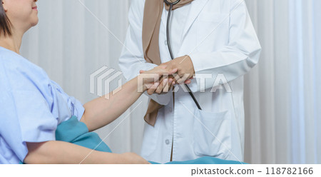 Muslim female doctor holding hand elderly patient sitting on the bed at hospital, takes care and cheerful concept. 118782166