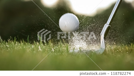 Golf club hits a golf ball. Drops of morning dew and grass particles rise into the air after the impact. 118782274